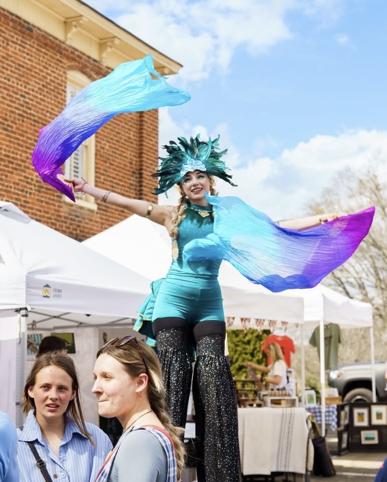 Teal colorful stilt walker with feather crown spinning silk fans while stilt walking