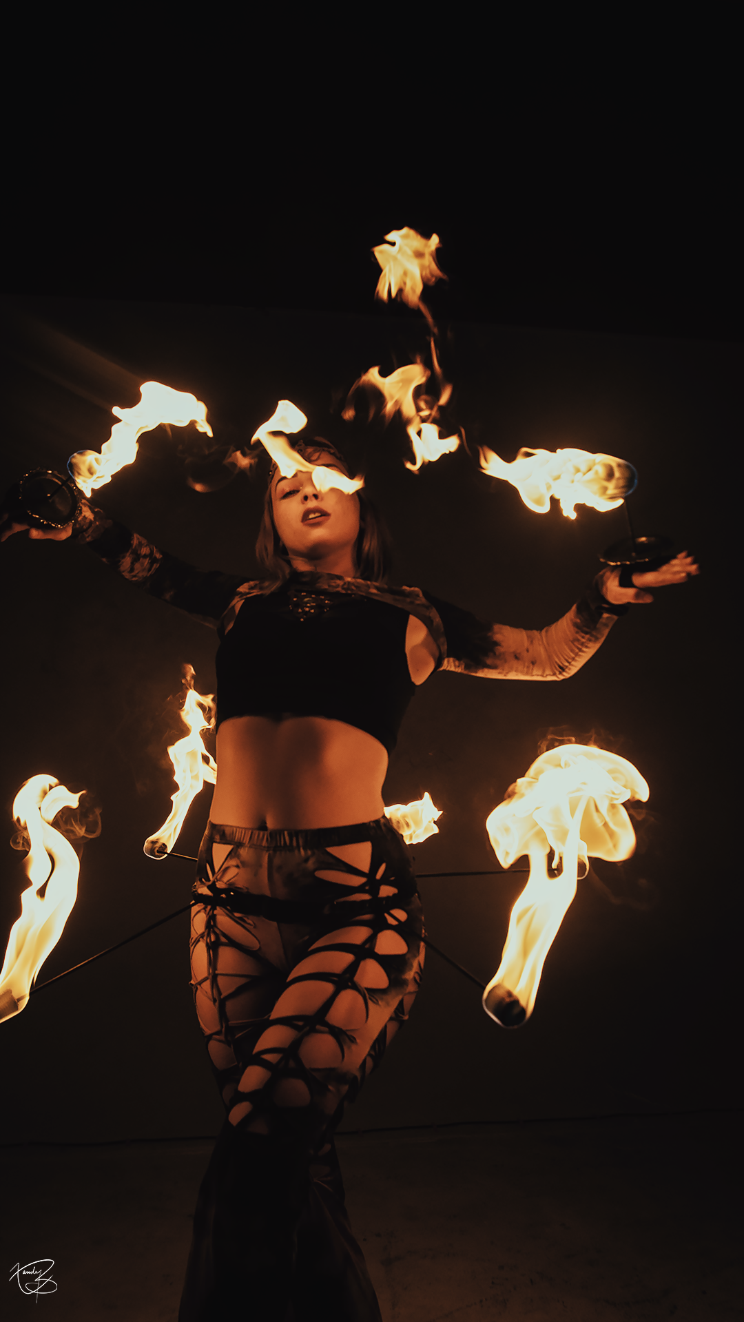 Pyro Priestess mid-performance wearing a belt on fire and dancing with fire palm toches.